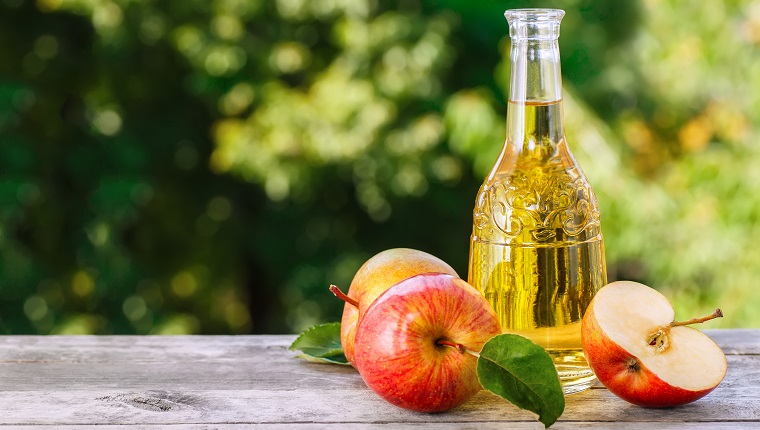 Apple cider, juice or vinegar in glass bottle on wooden table. Summer drink