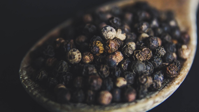 Black peppercorns on a wooden spoon - close up - macro photography