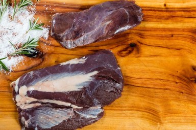 Raw emu meat slices on chopping board with herbs