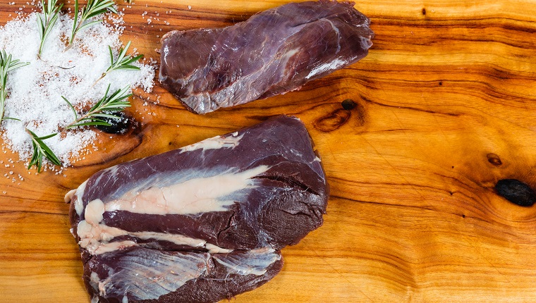 Raw emu meat slices on chopping board with herbs