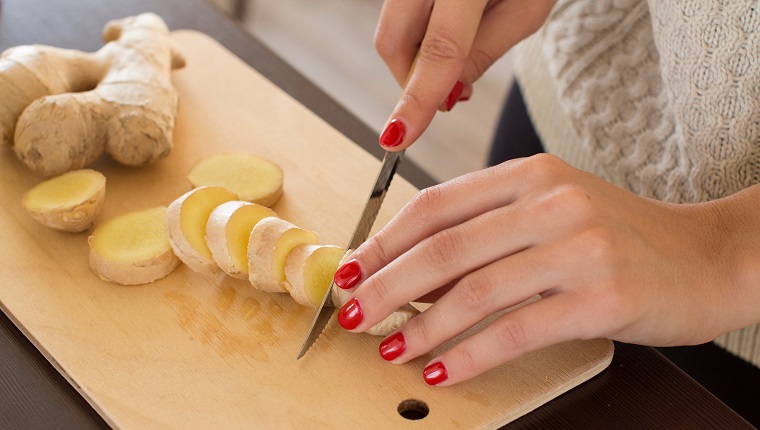 Cropped Hands Of Woman Cutting Ginger On Board In Kitchen At Home