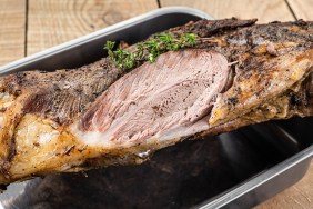 Whole oven roasted goat leg meat with thyme in a steel tray. Wooden background. Top view.