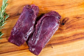 Raw kangaroo meat slices on chopping board with herbs