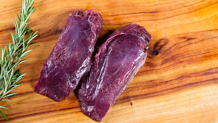 Raw kangaroo meat slices on chopping board with herbs