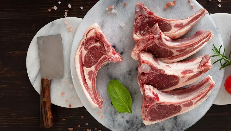 Fresh raw lamb on ribs on stone marble kitchen board on dark wooden background"t