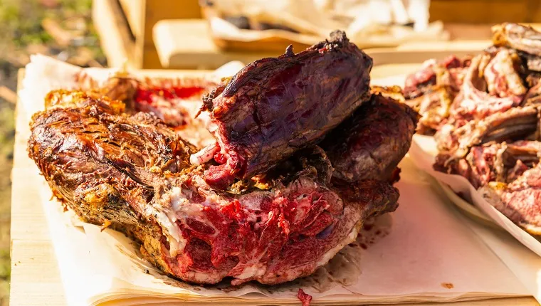 sliced large piece of moose meat on a wooden table, baked on the grill