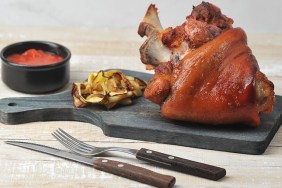 Baked pork knuckle on a wooden board. Ketchup sauce and grilled vegetables. Wood background. Close-up.