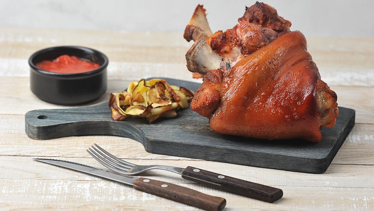 Baked pork knuckle on a wooden board. Ketchup sauce and grilled vegetables. Wood background. Close-up.