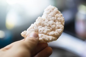 Rice cake broken in half, hand holding / giving food. Nice smooth colors creates a nice scene.