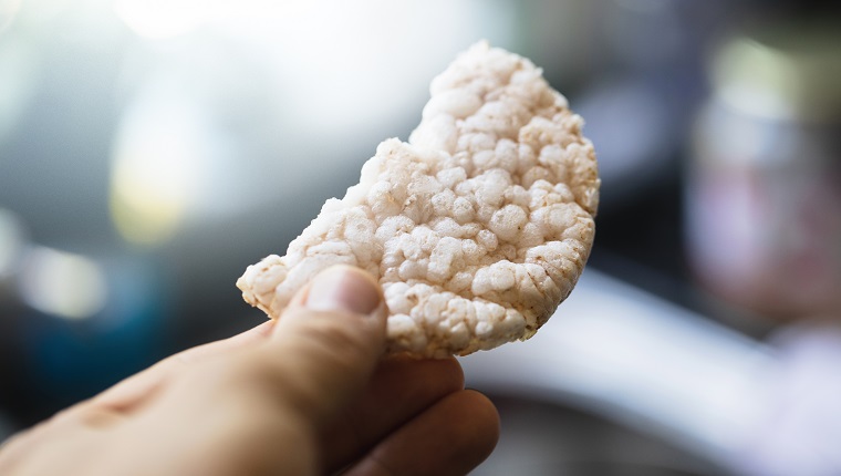 Rice cake broken in half, hand holding / giving food. Nice smooth colors creates a nice scene.