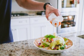 Close-up of unrecognizable white male pouring salad dressing onto salad