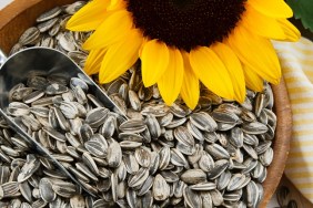 Nutritious sunflower seeds fill a wood bowl, accented with a metal scoop and yellow sunflower