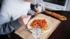 Close-up of unrecognizable white man eating pasta dish at home with Coton de Tuléar looking on
