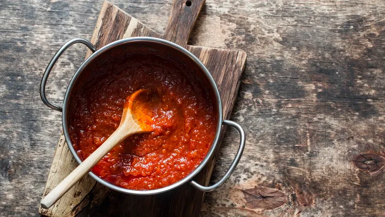 Classic homemade tomato sauce in the pan on a wooden chopping board on brown background, top view. Pasta, pizza tomato sauce. Vegetarian food