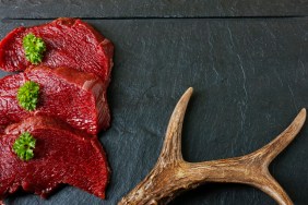Raw steak meat from roe deer on the bridlic chopping board. Roe deer antler as a decoration. Copy space for text.