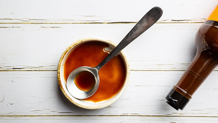 Worcestershire sauce in a bowl with spoon and bottle over white background, top view