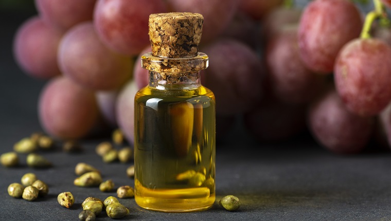 Grape seed oil in a glass jar and fresh grapes