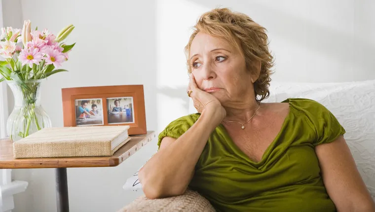 Sad senior woman in green t-shirt sitting on couch, pondering life after loss of pet