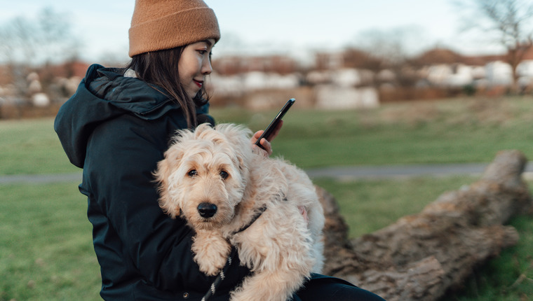 A woman scrolls on her smartphone while cradling her dog.