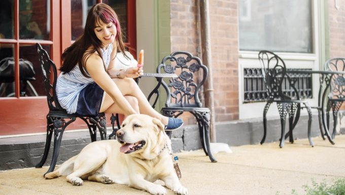 A woman smiles and pets her Labrador at an outdoor cafe.