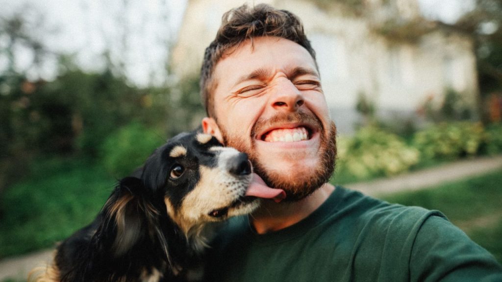 young man smiling while dog gives him kiss celebrating dog dads on Father's Day