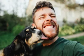 young man smiling while dog gives him kiss celebrating dog dads on Father's Day
