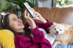 Young woman looking at TikTok dog trends with chihuahua on lap