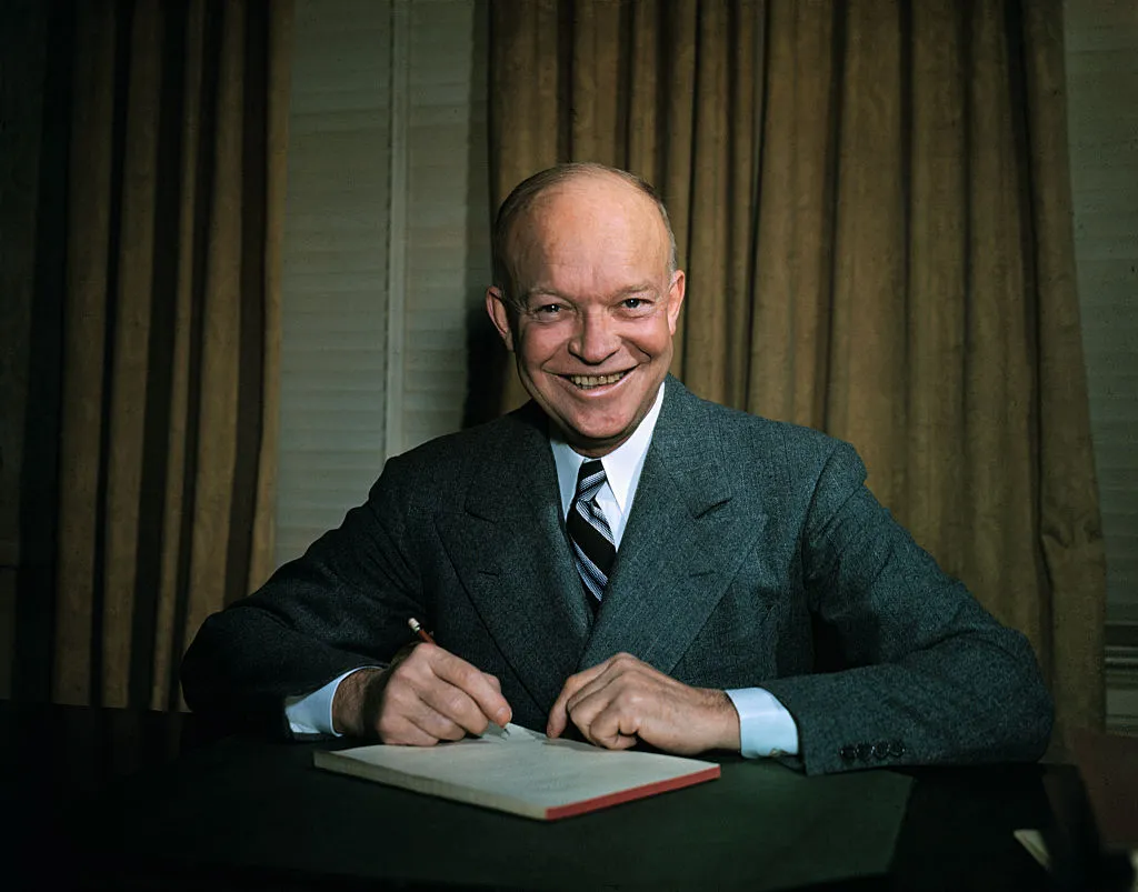 Dwight Eisenhower seated at desk with pen in hand.
