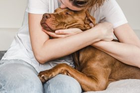 young woman hugging brown Pit Bull mix dog