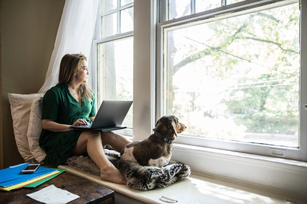 Woman working at home with dog, isolating him from other dogs as mystery dog illness spreads.