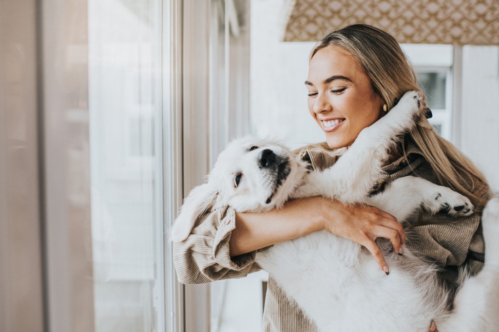 A young woman smiling while carrying her dog, one way to help your dog live longer