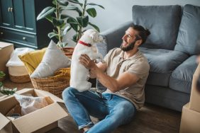 Young man moving in pet-friendly apartment. He is happy and playing with his pet dog.