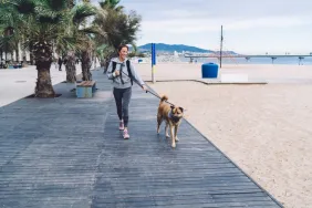 Lady walking dog on a leash along a boardwalk during the day, exactly what Mission Bay dog owners not supporting boardwalk dog walking ban want.