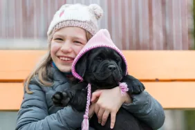 Portrait of a girl and her black Labrador puppy wearing a hat like the Labrador Retriever therapy dog in a New York school.