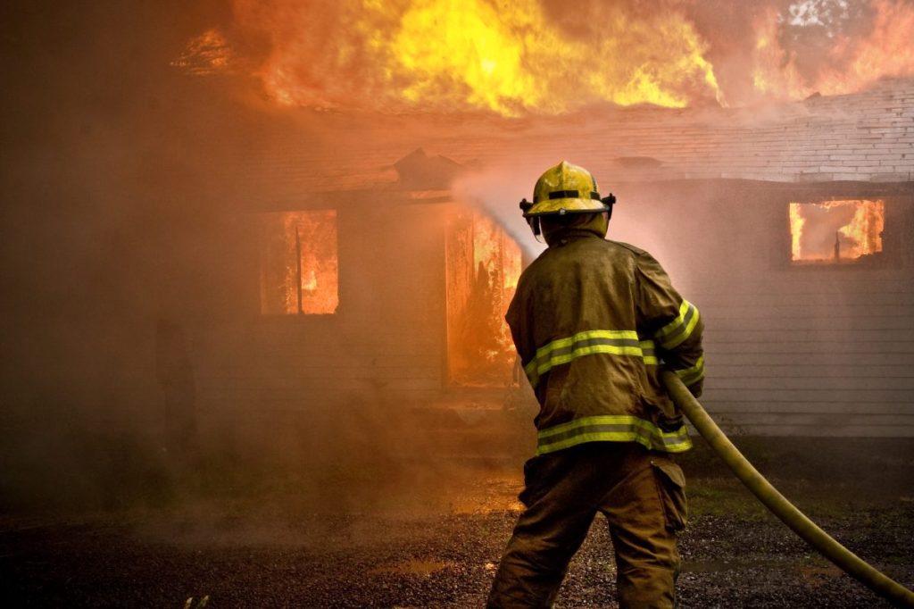 Firefighter spraying water at a house fire ; 17 Dogs Die in Fire on Thanksgiving