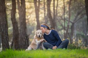 Woman kissing her Golden Retriever dog in a forest, highlighting the potential benefits of dog ownership on reducing dementia.