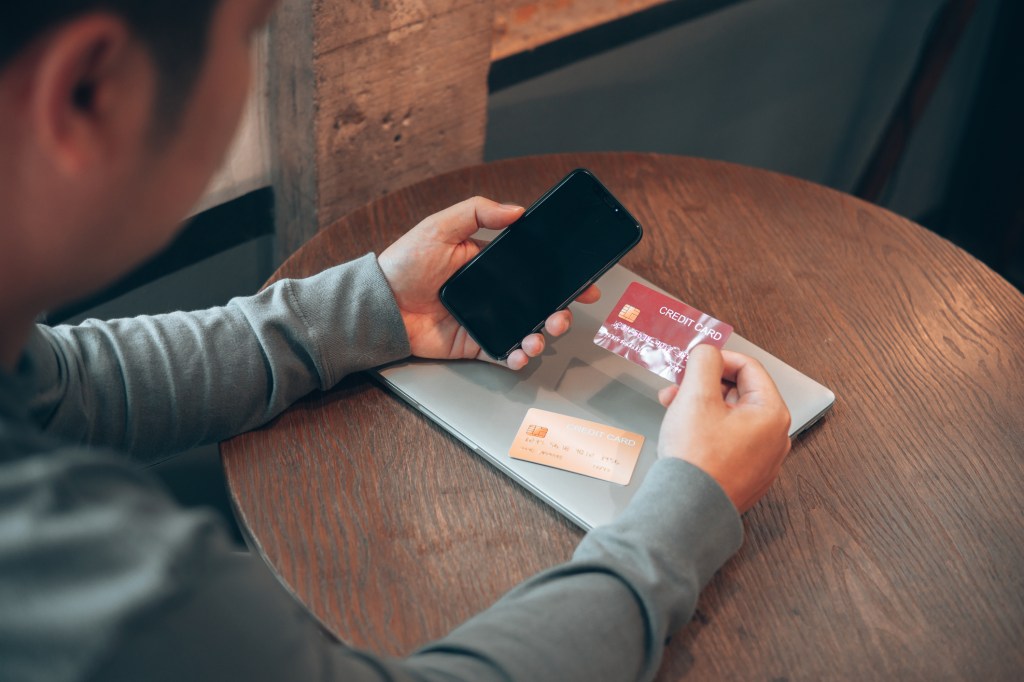 A man holding his phone and credit card, similar to the people who fall victim for online puppy scams and share their credit card information.