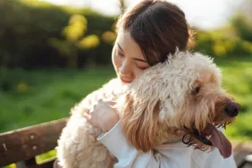 Young Asian woman sitting hugging her Goldendoodle dog, an emotional support animal, in the park.