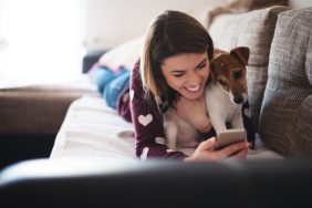 A woman using her phone with her dog, similar to the people who are buying puppies online and becoming victims of online puppy scams.