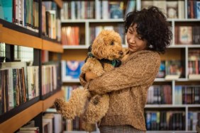 A happy student carrying a brown therapy dog in the library, like the therapy dogs with the Love Dog Adventures