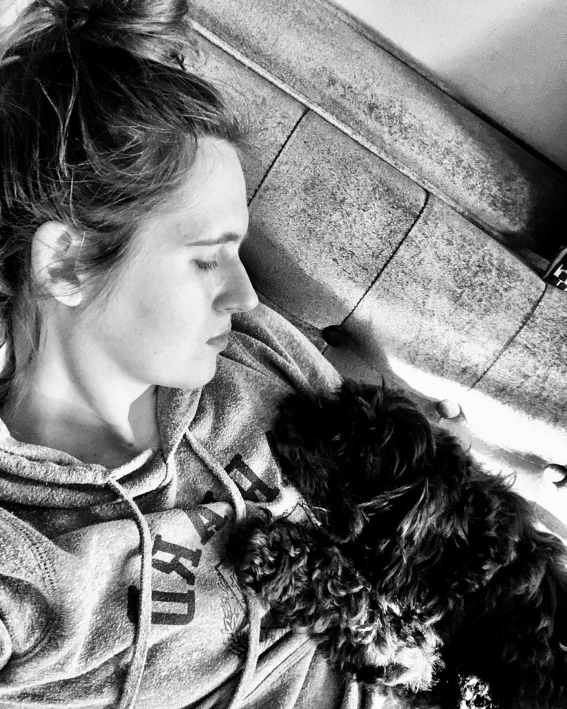 Jenna Wadsworth resting on couch with Washington, a Schnoodle, on her chest.