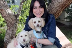 Actress Rena Sofer sitting on a bench holding two small white dogs, Rena Sofer's dog, Alfie,has died of cancer