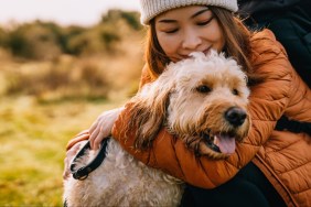 Young Asian woman hugging her dog while hiking in autumn nature. Emotional support and mental wellbeing.
