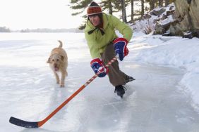 Man playing hockey on frozen lake with dog running beside him