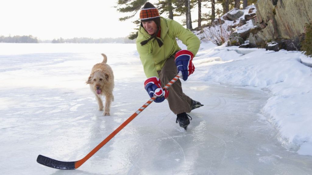 Man playing hockey on frozen lake with dog running beside him