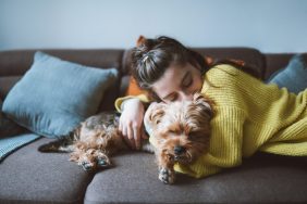 A shot of a young woman hugging her little dog while lying down on the sofa in her living room.