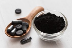 Activated charcoal powder for dogs in a glass bowl with capsules and tablets on a spoon on white wooden background, used to treat poisoning.