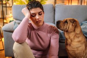 Stressed young woman sitting on the floor at home, with her Chinese Shar-Pei sitting next to her worried. Recent study found dogs smelling rising stress levels in humans can affect their decision-making and mood.