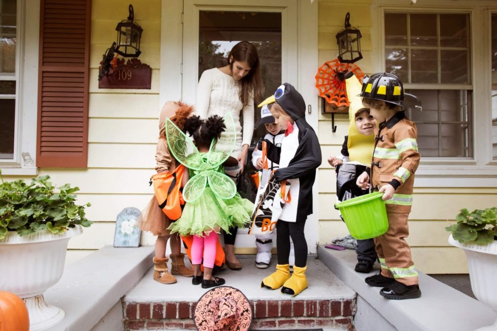 Woman offering Halloween candy to trick-or-treaters outside.