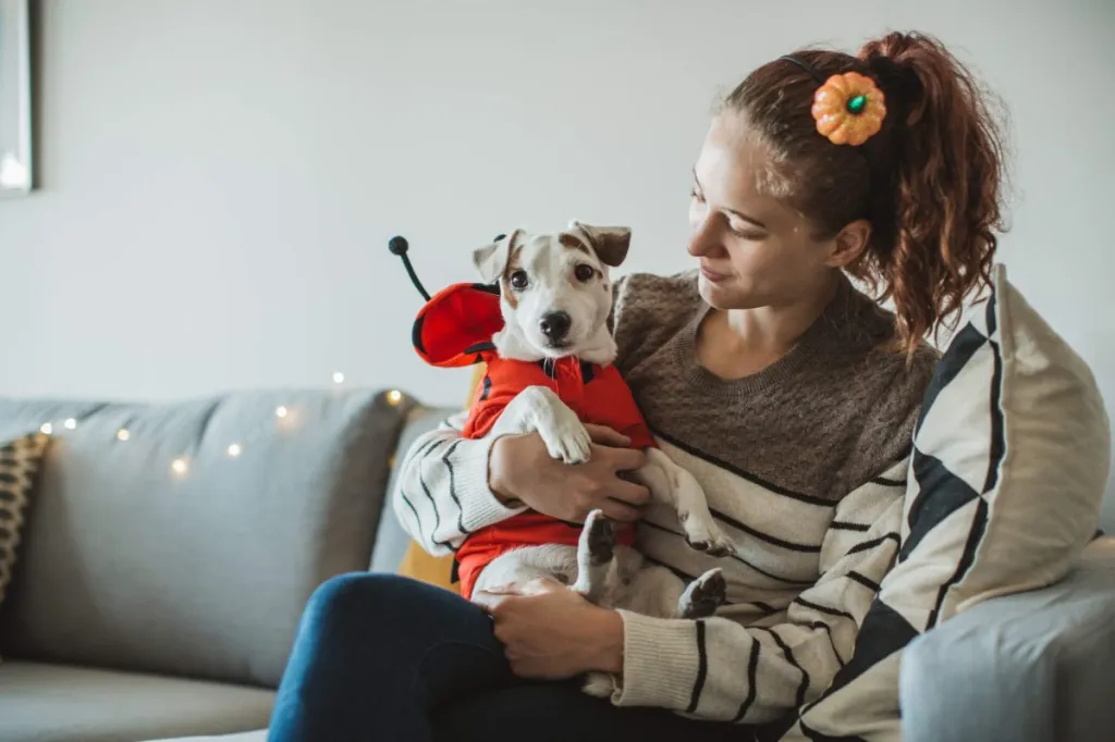 Young woman celebrating Halloween at home with her dog in costume.